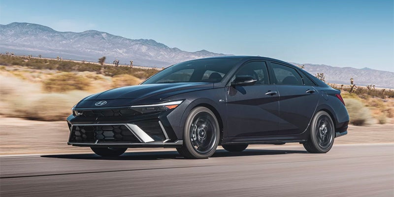 Dark gray Hyundai Elantra N sport sedan in motion on an open road, featuring sharp body lines