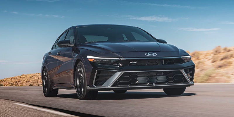 Front view of a dark gray Hyundai Elantra N sedan driving on a highway, highlighting the signature grille