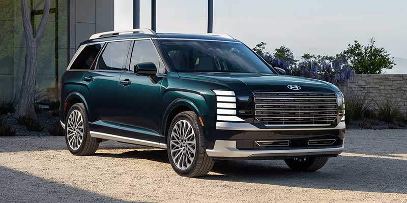 Front three-quarter view of a dark green Hyundai Palisade SUV parked outdoors near a modern building