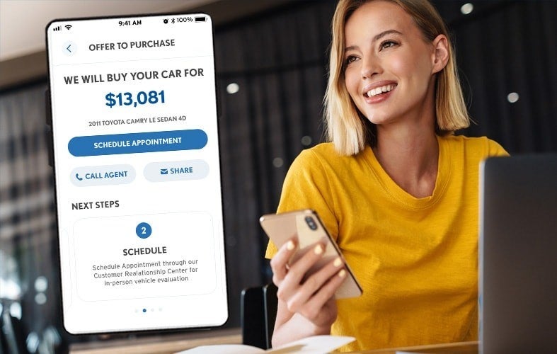 Smiling woman views a car purchase offer for $13,081 for a 2011 Toyota Camry on her smartphone